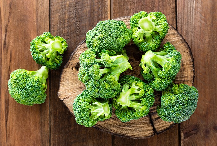 Pieces of raw broccoli on top of a tree bark chopping board. 