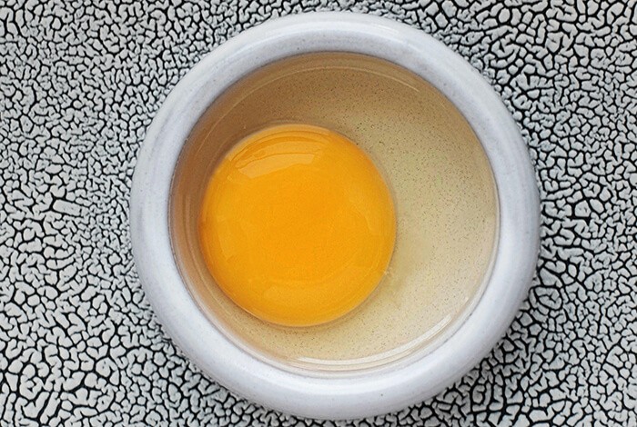 A raw egg in a ceramic bowl.