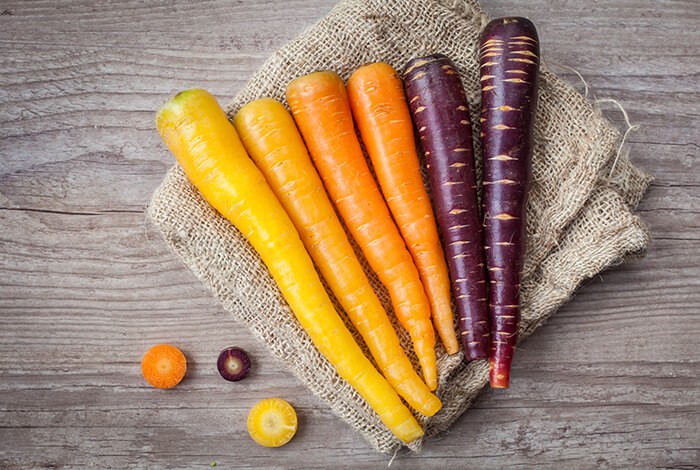 Carrots of different colors are placed on top of a burlap.