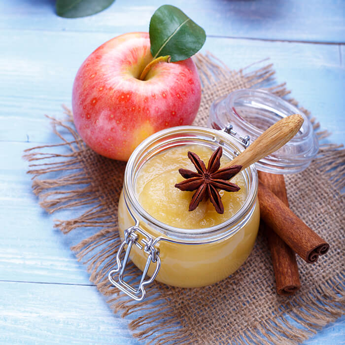 A jar of cinnamon applesauce, an apple, anise, and cinnamon sticks.