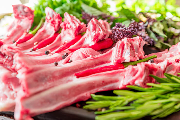 Raw goat chops surrounded by herbs and vegetables.
