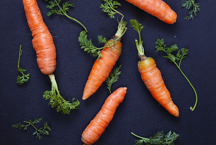 Raw carrots with leaves placed on top of a dark blue surface.