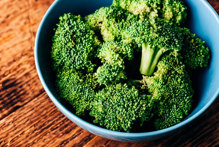 Pieces of raw broccoli in a blue bowl.