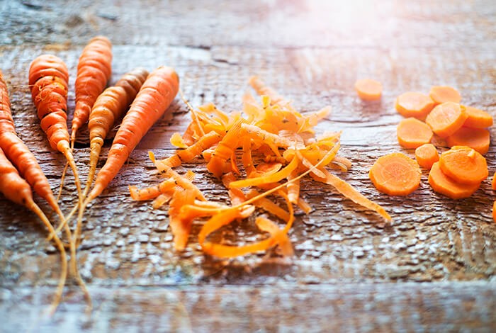 Groups of raw carrots, peeled carrot skin, and sliced carrots. 