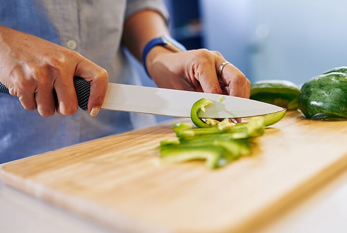 A person is slicing a green bell pepper.