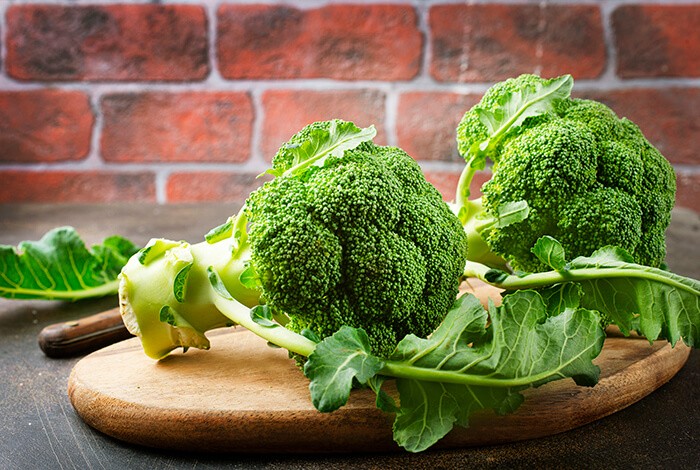 Two broccoli heads on a wooden chopping board.