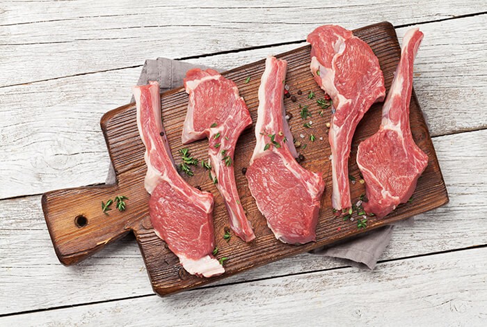 A rack of herb lamb displayed on a wooden chopping board.