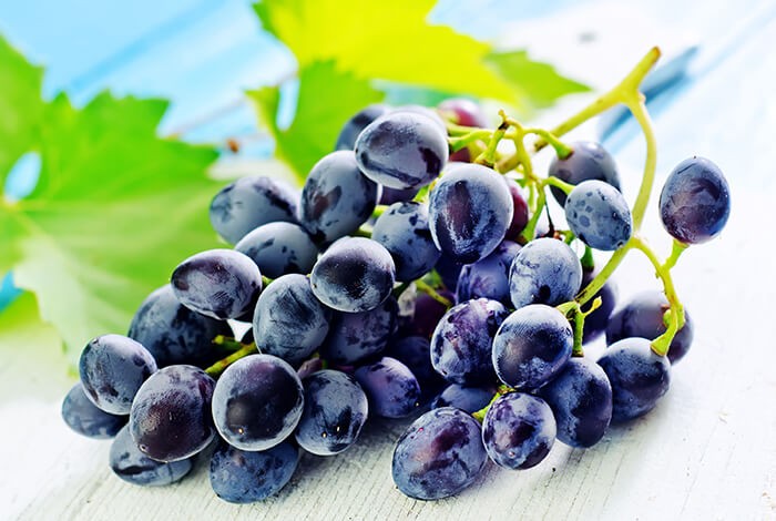 A bunch of dark grapes placed on a white wooden surface.