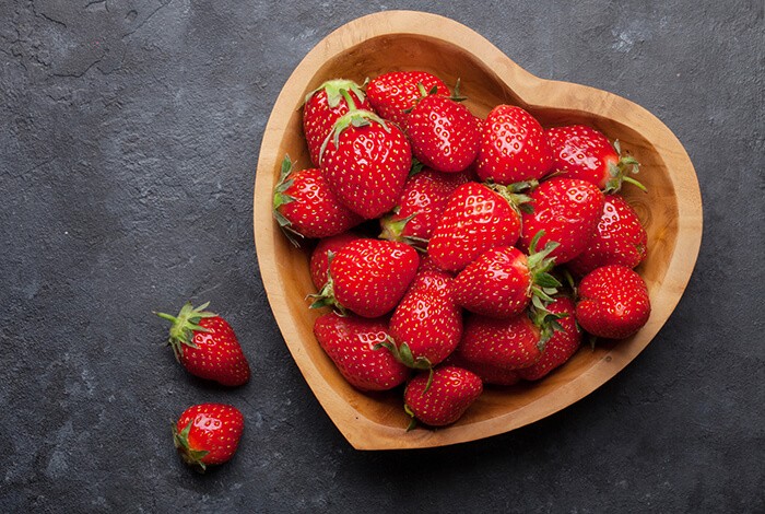 Strawberries placed in a heart-shaped wooden bowl.