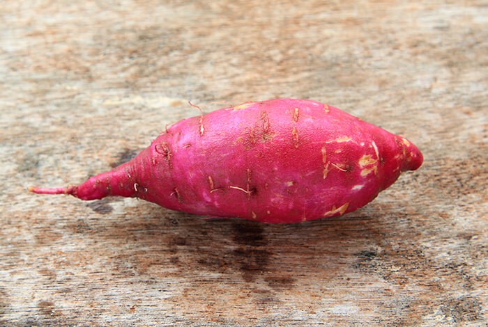 A raw sweet potato on a wooden surface.