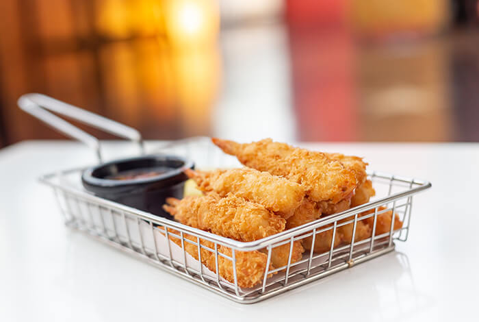 Pieces of breaded shrimp and sauce dip in a steel basket.