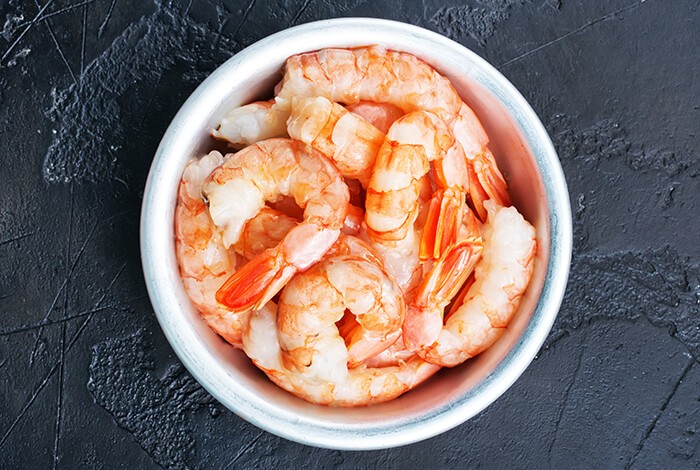 Pieces of peeled, cooked shrimp in a tin bowl.