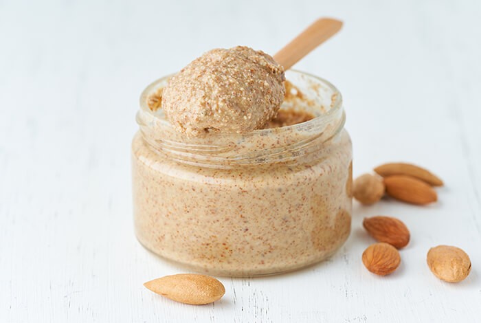 A small jar of almond butter with a few pieces of almonds beside it.