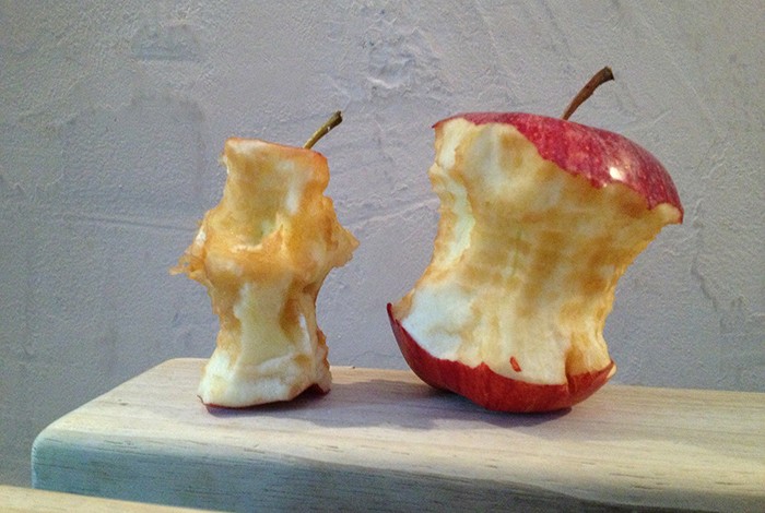 Two eaten apples on top of a bench.