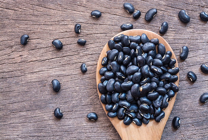 A wooden spoon filled with raw black beans.