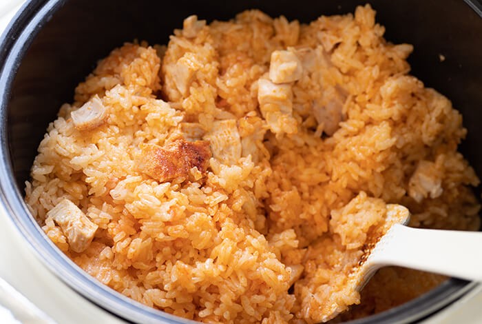 A rice pot filled with cooked white rice and mixed with chicken bits and tomato sauce.