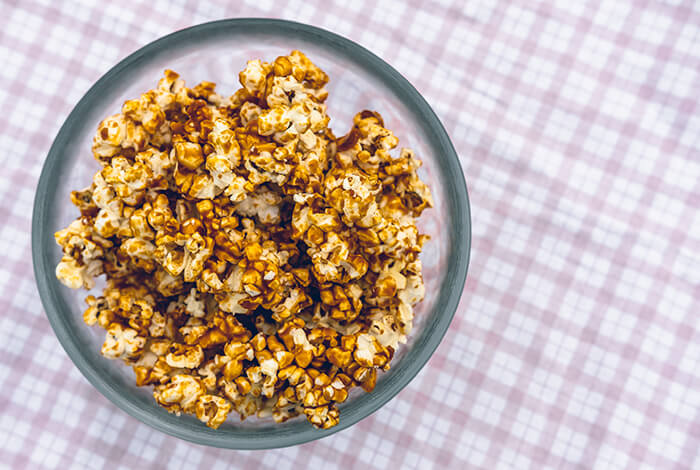 A bowl of caramel popcorn on top of a plaid tablecloth.