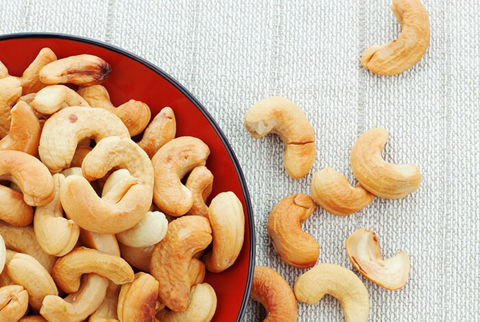 Toasted cashews placed on a red ceramic plate.