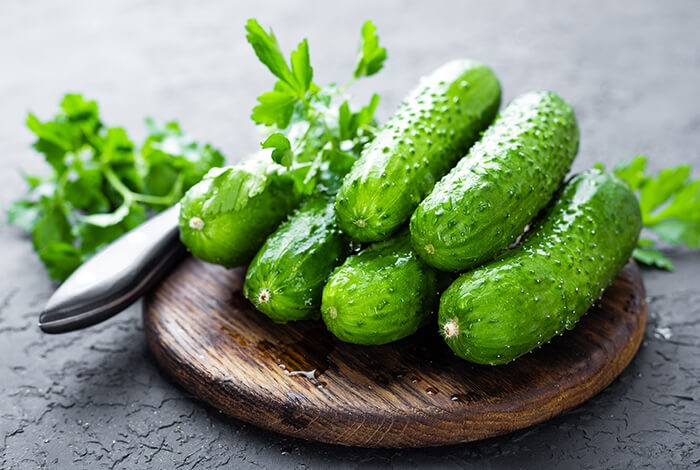 Six cucumbers on top of a round, wooden cutting board with a knife on the side.