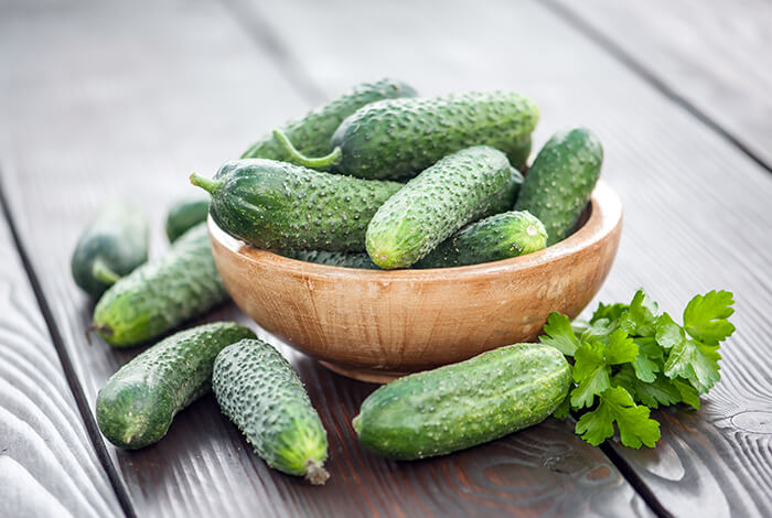 A wooden bowl filled with small cucumbers.