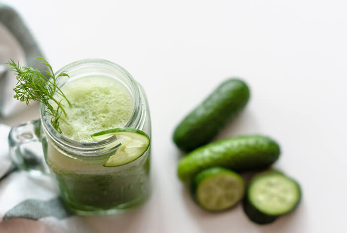 A cucumber smoothie in a mason jar and slices of cucumbers beside it.