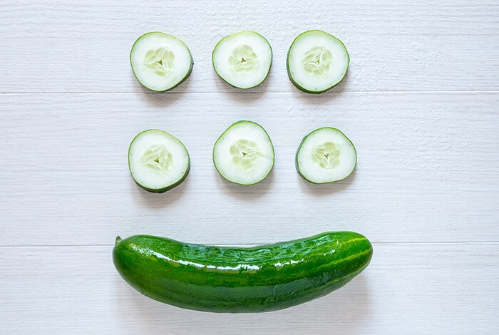 Six slices of cucumber and a wet cucumber on a white wooden surface.
