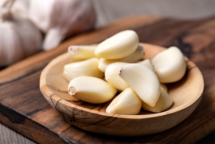 Raw garlic cloves on a wooden bowl.