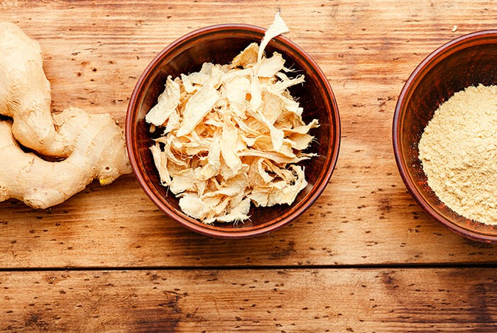 Two bowls of dried ginger flakes and ground ginger, and a ginger root. 