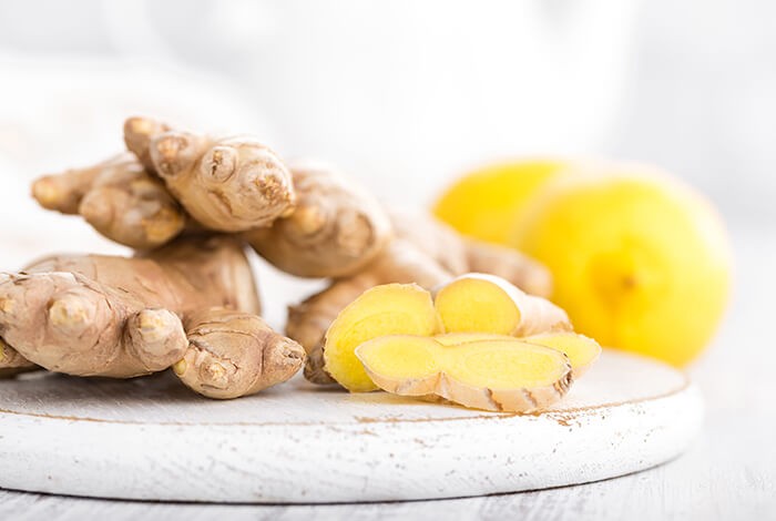 Pieces of sliced ginger on a white wooden chopping board with lemons in the background.