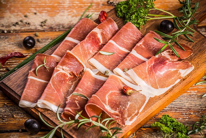 Pieces of dry-cured ham on a wooden chopping board. 