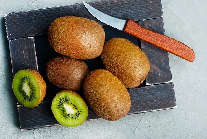 Kiwi fruits and a knife on a wooden board. 