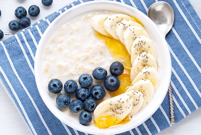 An oatmeal porridge topped with sliced bananas, blueberries, honey, and chia seeds.