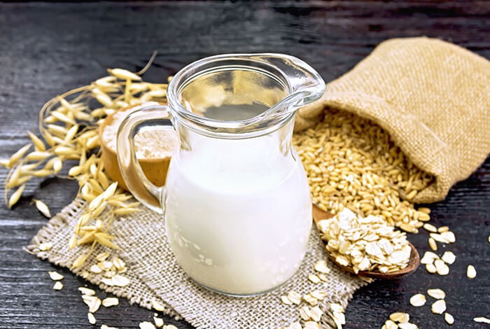 A glass pitcher filled with milk and a burlap sack filled with oats. 