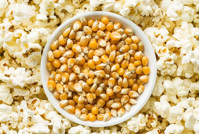 A bowl of popcorn kernels on top of popcorns. 