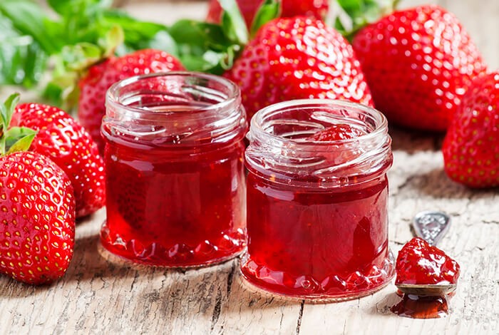 Two small jars filled with strawberry jellies with strawberry fruits in the background.