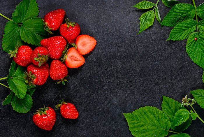 Strawberries and their leaves placed on top of a dark blue-colored surface.