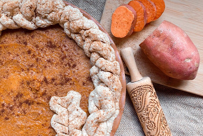 A sweet potato pie with raw sweet potatoes on the side.