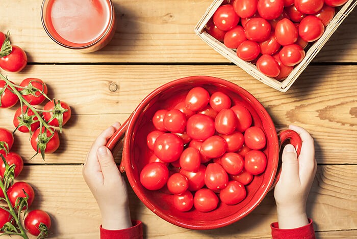 A glass of tomato juice, a bowl of tomatoes, and a native tray of tomatoes.