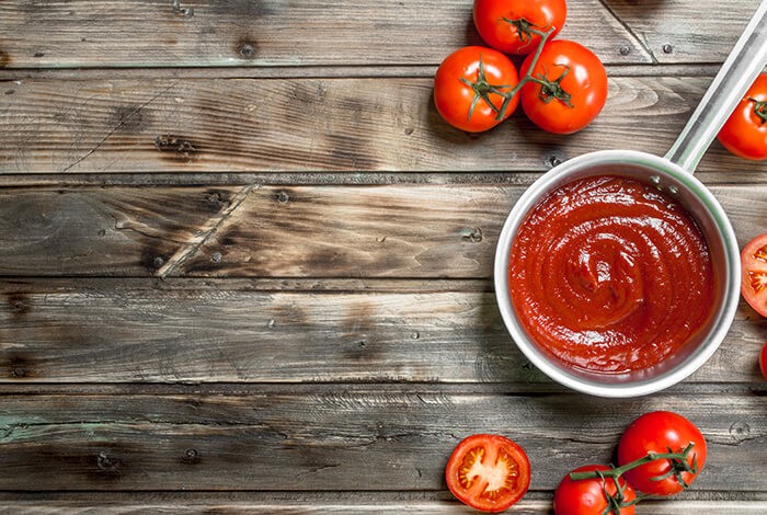 A small pan filled with tomato sauce and some pieces of red tomatoes.