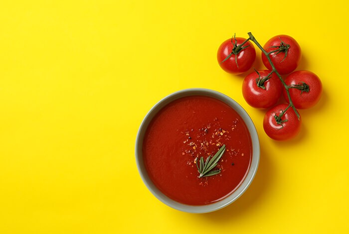 A bowl of tomato soup and a bunch of tomatoes.