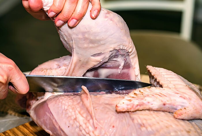 A raw turkey leg being sliced.