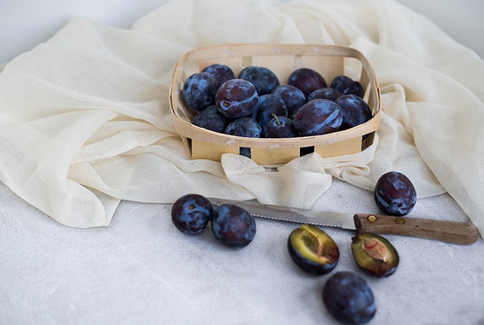 A small basket of plums and a jagged knife.