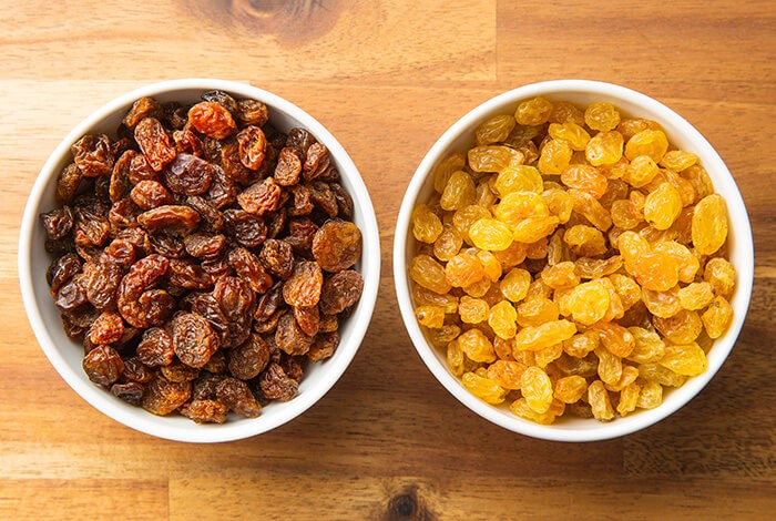 Two white bowls, one filled with dark raisins and another with white raisins.