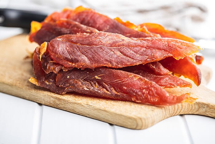 Chicken jerky for dogs placed on a wooden chopping board.