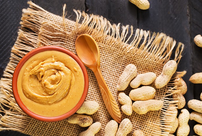 A bowl of peanut butter surrounded by peanuts.