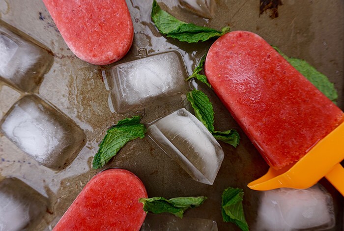 Homemade watermelon ice pops with mint leaves and iced cubes.