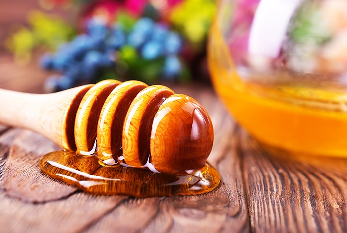 A honey dipper with honey placed on a wooden surface.