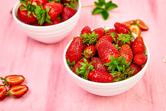 Two white ceramic bowls filled with strawberries.