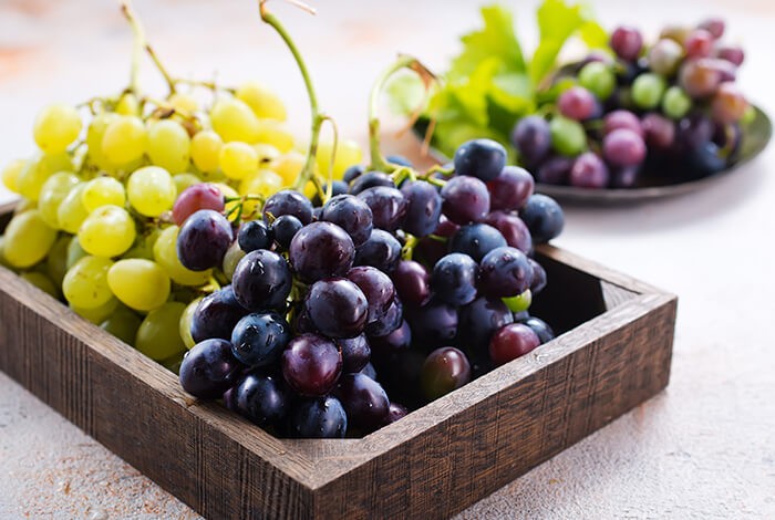 Bunches of green and dark grapes placed in a wooden, rectangular tray. 