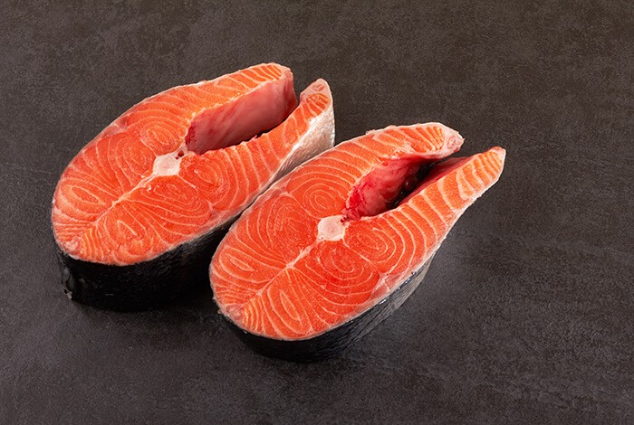 Two slices of raw salmon on a smooth surface.
